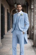 Man wearing a light blue morning suit with waistcoat standing in a classic stone corridor.
